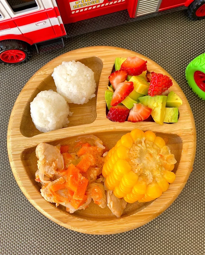 Plato de bambú con bolitas de arroz, pollo con zanahoria, mazorca y ensalada de aguacate con fresas.